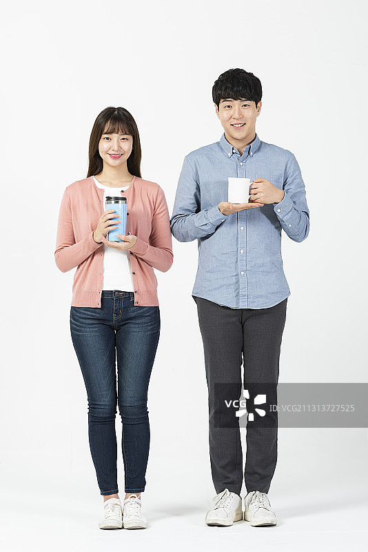 两名大学生拿着水杯和马克杯在白色背景下微笑图片素材