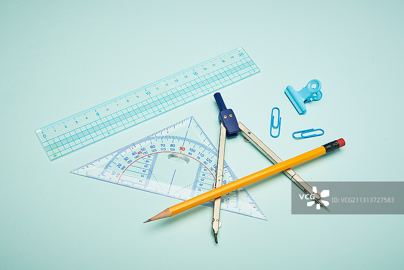 绿色背景上的学习用品，如圆规、尺子、纸夹和铅笔图片素材