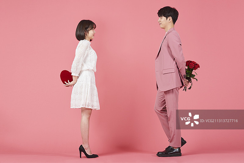 粉色背景下，情侣手捧心形礼盒和花束深情对视图片素材