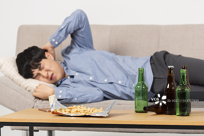 醉酒男子躺在沙发和桌子上，旁边有啤酒、烧酒和小吃图片素材