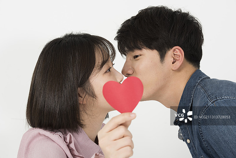 大学生情侣在白色背景上手持心形纸亲吻图片素材