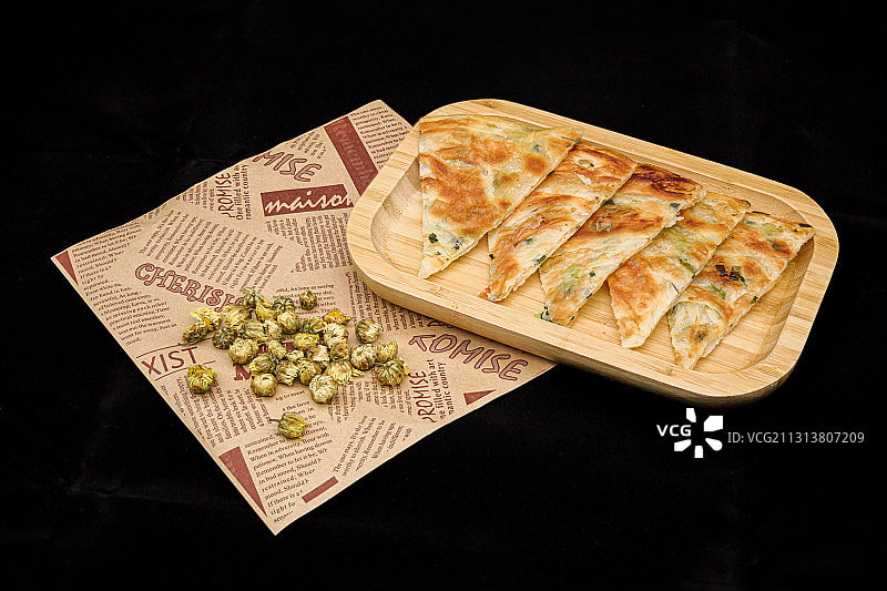 纯黑色背景里，一个木碟子上放着几块北方的特色小吃葱油饼图片素材