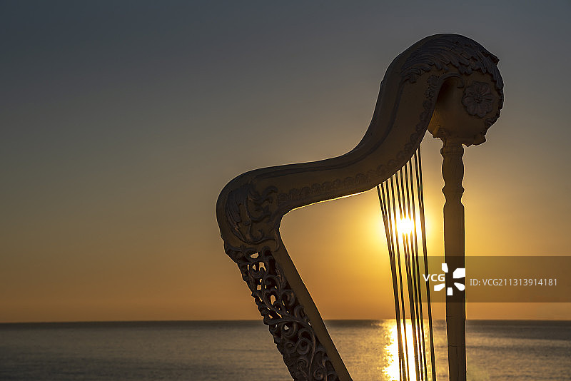 清晨从海面上升起的太阳照射在竖琴雕塑的琴弦上图片素材