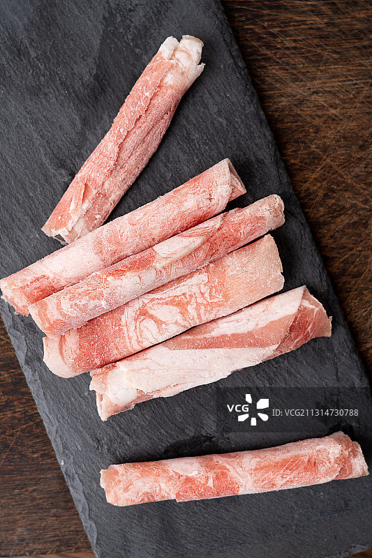 褐色厚实黑岩板上的鲜美肥羊生鲜羊肉卷以及火锅配菜蘸料图片素材