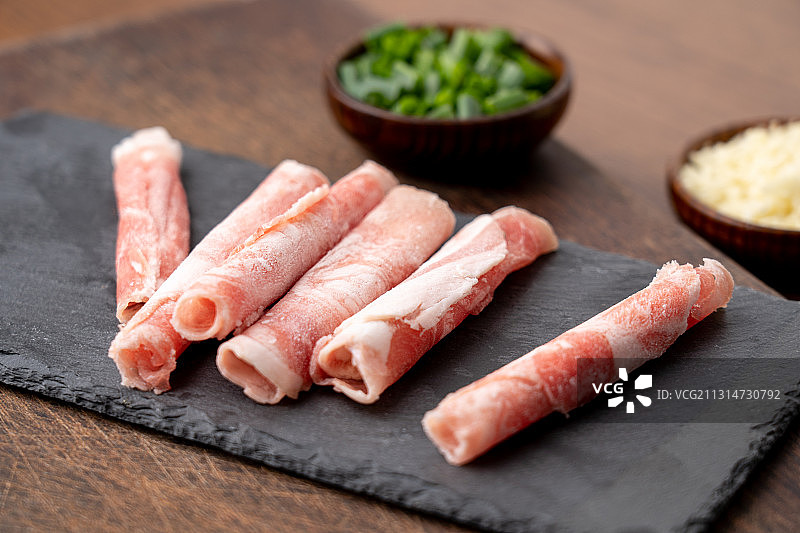 褐色厚实黑岩板上的鲜美肥羊生鲜羊肉卷以及火锅配菜蘸料图片素材