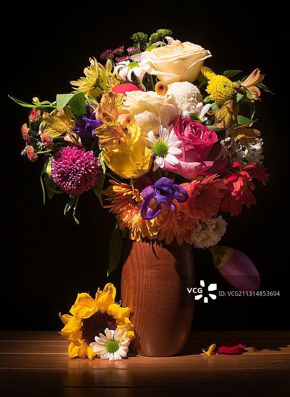 棚拍暗背景木质桌子的花瓶和花朵以及书本和花瓣图片素材