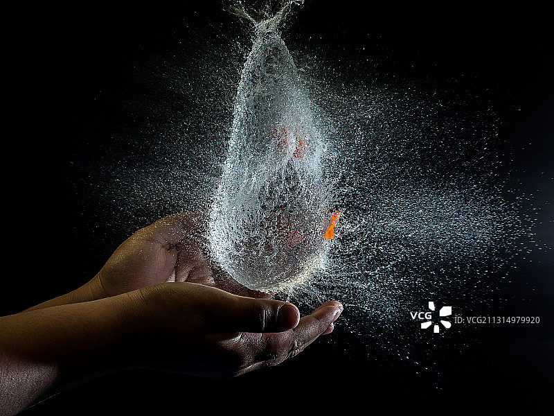 在黑色背景下拿着爆炸水球的局部手部照片图片素材