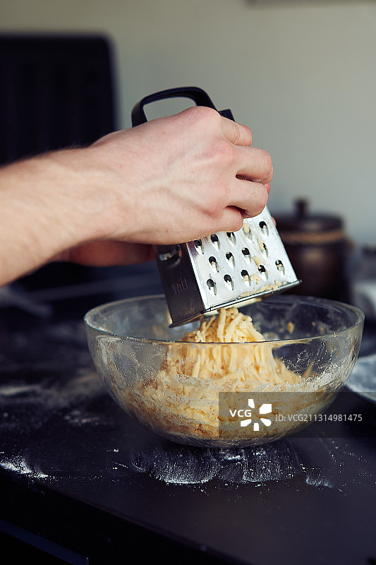男人在厨房里把奶酪磨碎到碗里的特写镜头图片素材