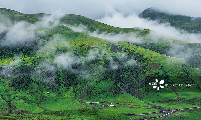 四川甘孜县的高原山地，云雾缭绕的山梁下有几户人家图片素材