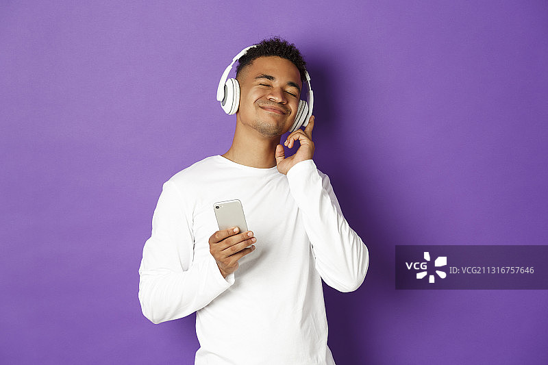 靠在紫色背景墙上使用手机的年轻男人图片素材