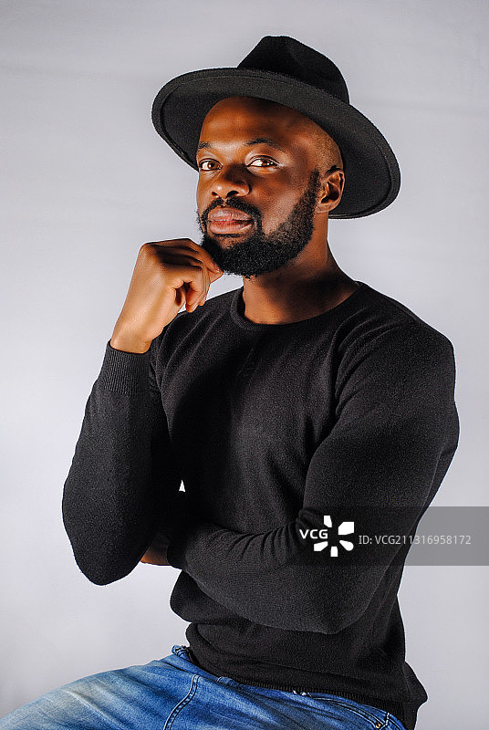 靠在灰色背景上的戴帽子年轻男人肖像，南非约翰内斯堡图片素材