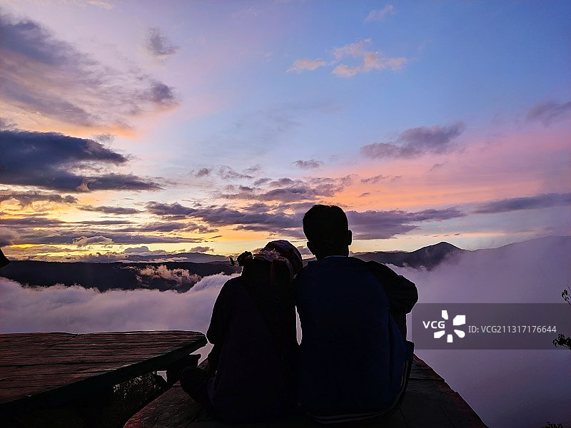 日落时分，情侣坐在印度尼西亚伦邦山上，以天空为背景的背影图片素材