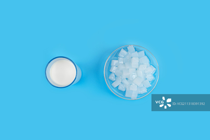 蓝色背景下玻璃杯里的椰汁和碗中的椰肉块图片素材