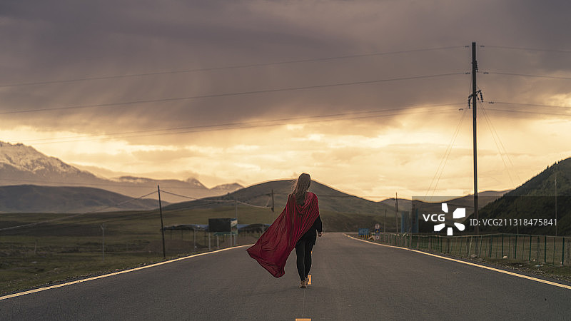 乌云密布穿红色披风的女人背影行走在公路中央图片素材