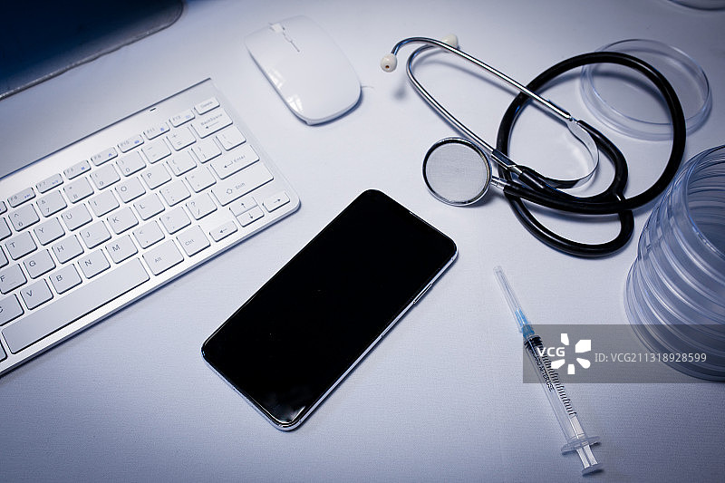 医生诊室里的书桌，配有智能手机、电脑、键盘、注射器和听诊器图片素材