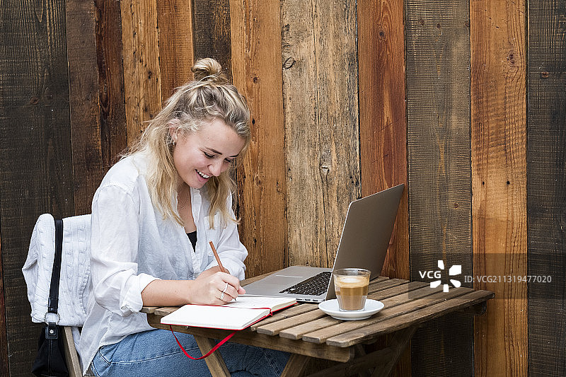 英国沃灵顿，年轻金发女子在咖啡馆用笔记本电脑远程工作图片素材