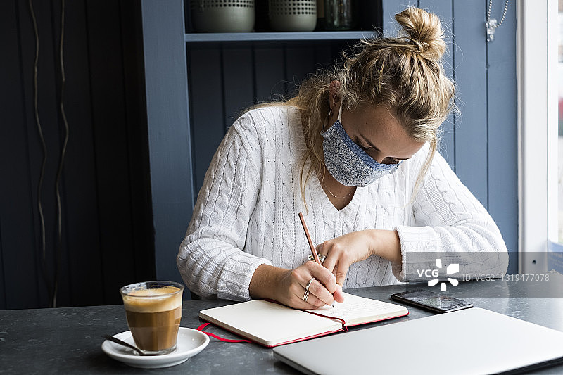 英格兰沃灵顿，戴口罩的女人独自坐在咖啡馆的桌子旁，远程工作图片素材