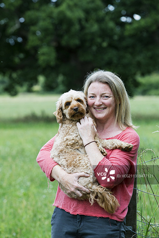 英国沃灵顿，微笑的女人抱着小鹿色卡瓦蒲犬图片素材