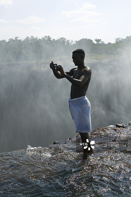 赞比亚维多利亚瀑布，站在悬崖边拍照的男人图片素材