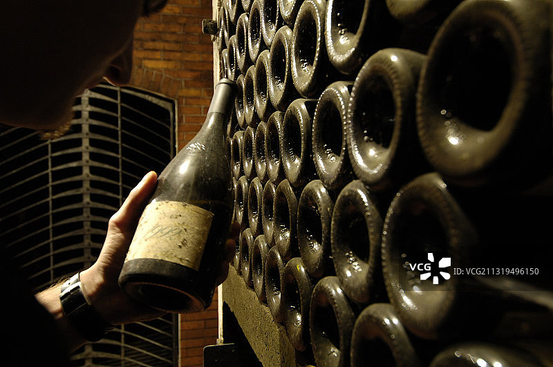男子在葡萄酒窖里拿着一瓶陈年葡萄酒（意大利，泰尔兰）图片素材