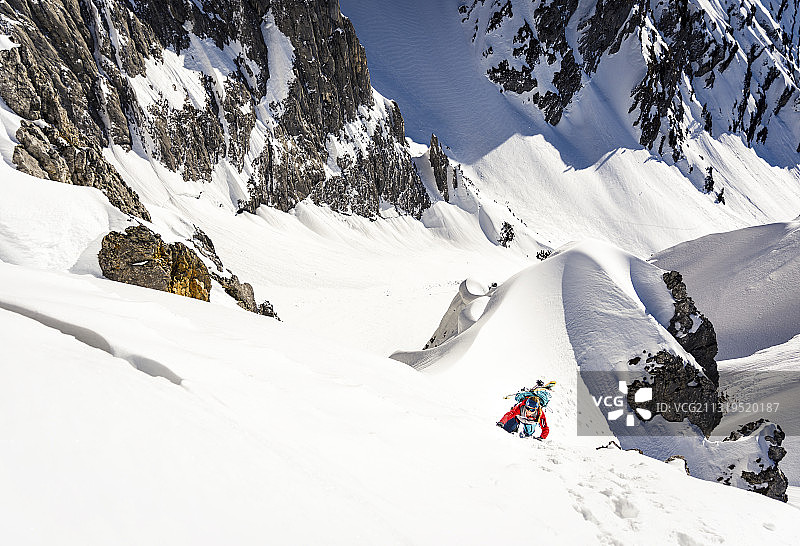 年轻女子在冬季山区攀登，脚穿冰爪，手持冰镐图片素材