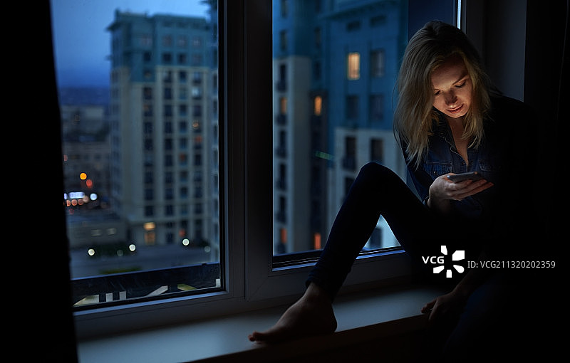 女人坐在窗台上玩手机图片素材