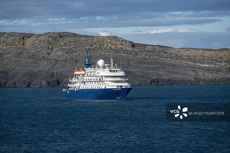 海精灵号探险邮轮（波塞冬探险队）在挪威斯匹次卑尔根岛的贫瘠山丘背景下，等待着岸上的乘客返回图片素材