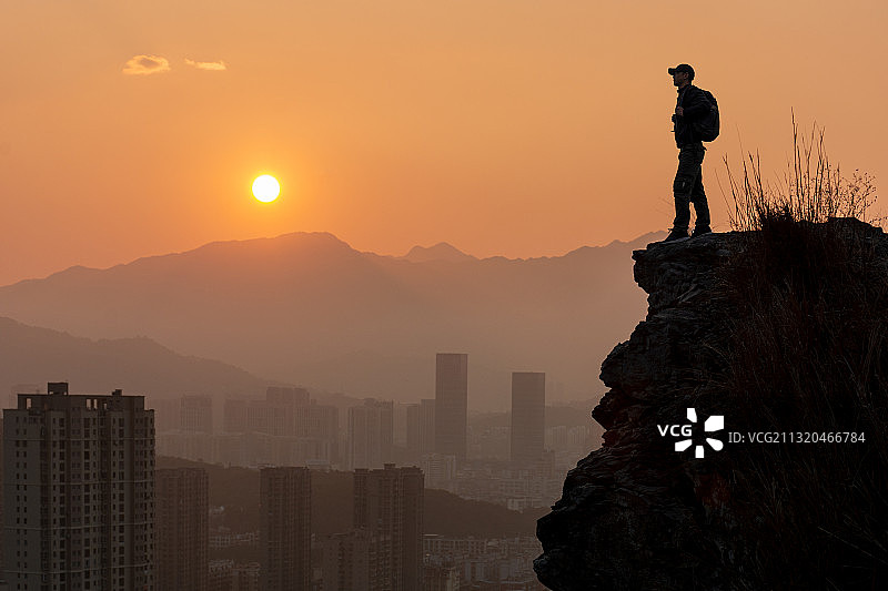 夕阳下一个人站在城市周边的岩石上图片素材