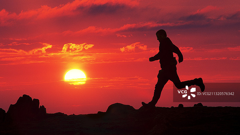 日落时分在红色山坡上奔跑的男人，英国湖区图片素材