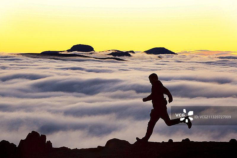 英国坎布里亚郡湖区红色山坡上的盖博山，因逆温形成的谷云，以及一名跑步的男子图片素材