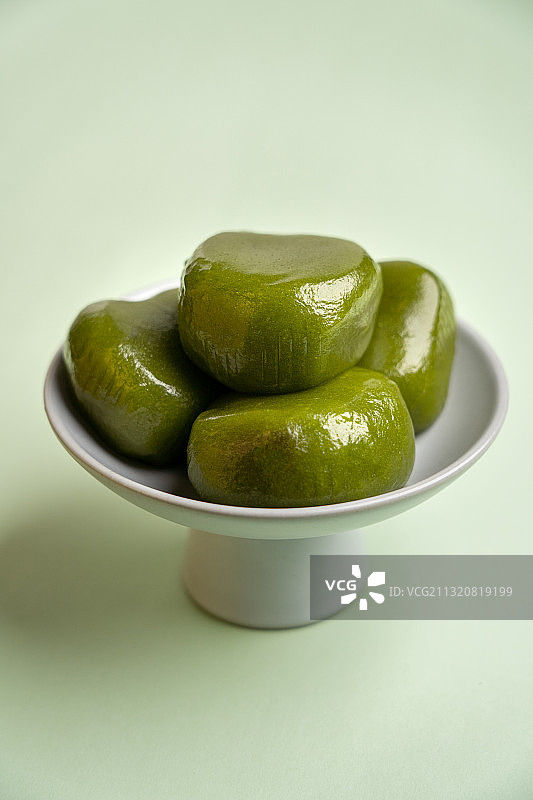 绿色纯色背景留白陶瓷高脚茶点盘上的绿色食品青团图片素材
