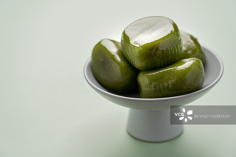 绿色纯色背景留白陶瓷高脚茶点盘上的绿色食品青团图片素材