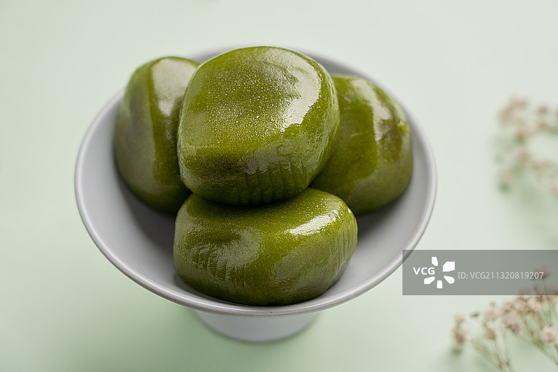 绿色纯色背景留白陶瓷高脚茶点盘上的绿色食品青团图片素材