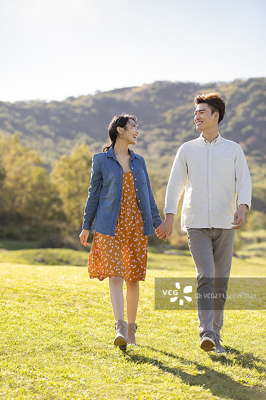 快乐的年轻情侣手牵手在草地上散步图片素材