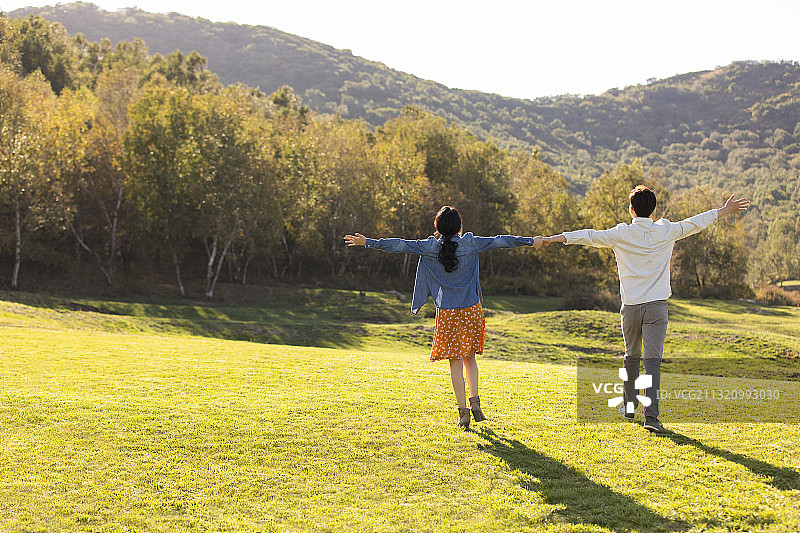 快乐的年轻情侣手牵手在草地上散步图片素材