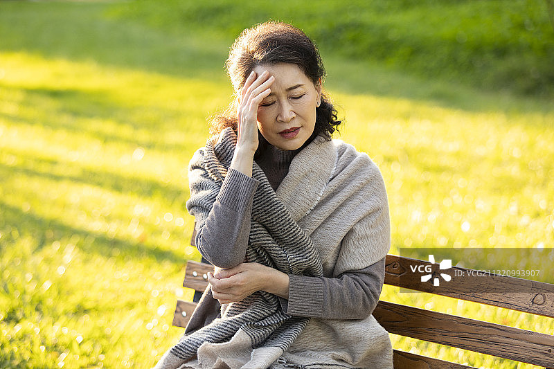 老人头疼坐在公园长椅上图片素材