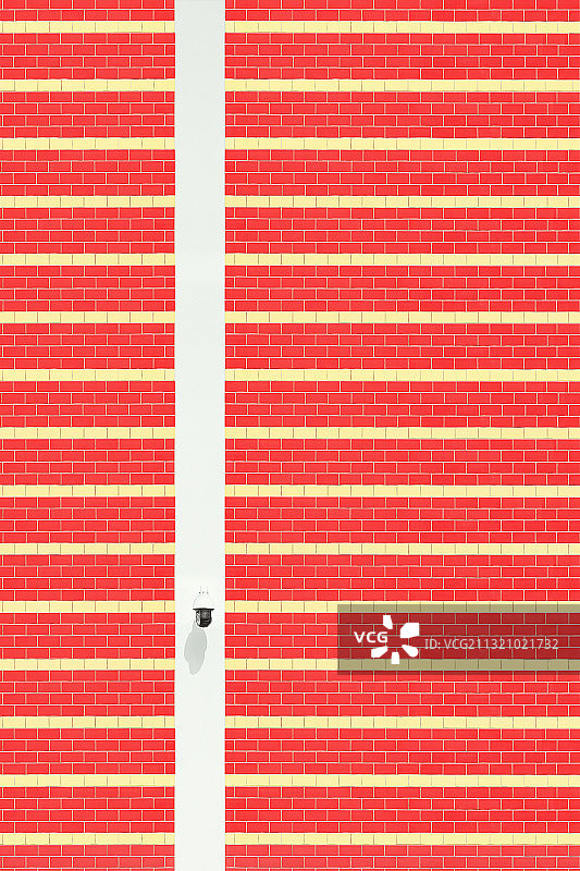 红色和橙色横纹墙壁上一个白色监控摄像头图片素材