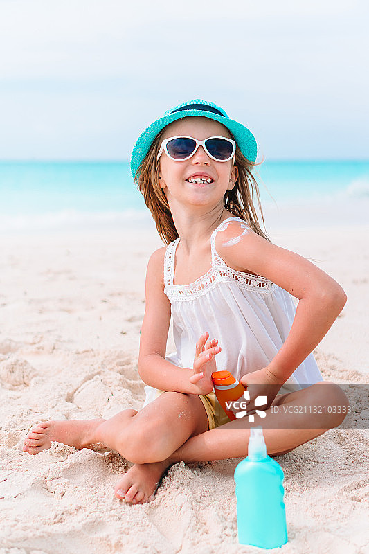 坐在热带海滩，拿着防晒霜的小女孩图片素材