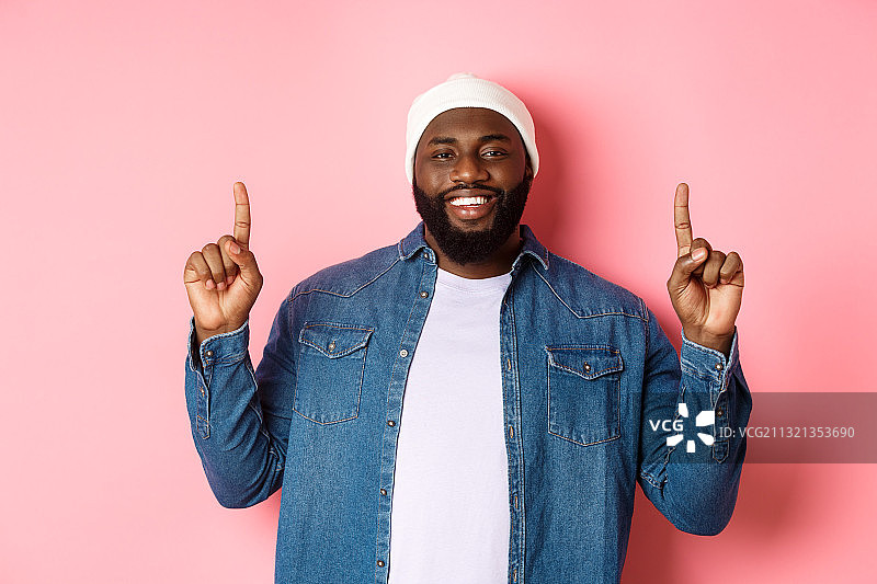 靠在粉色背景上手势的微笑年轻男人的肖像图片素材