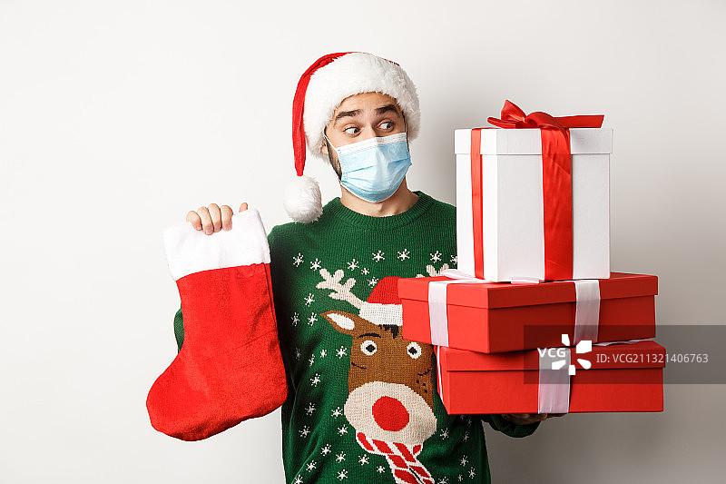 戴着圣诞帽，手持礼品盒，在白色背景前微笑的女人肖像图片素材