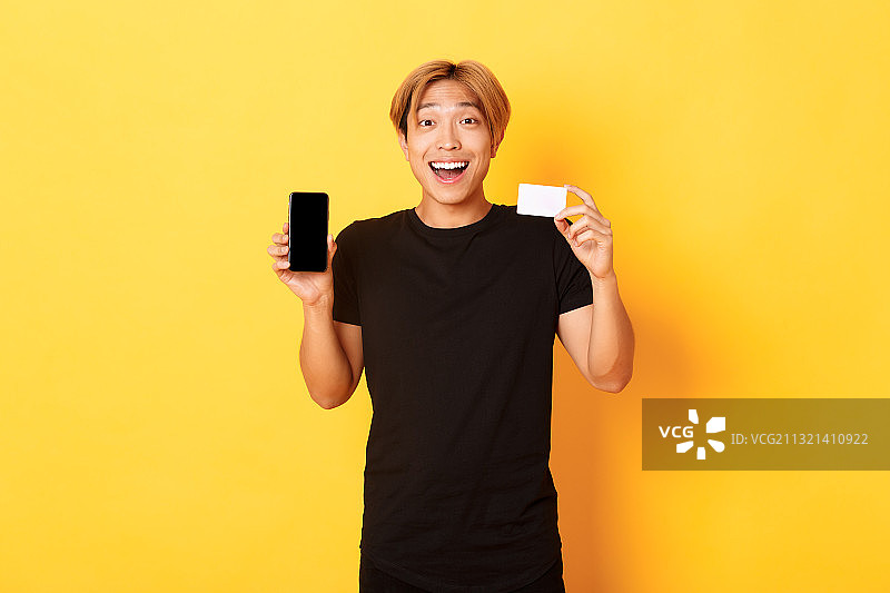 微笑的女人在黄色背景下手持信用卡的肖像照图片素材