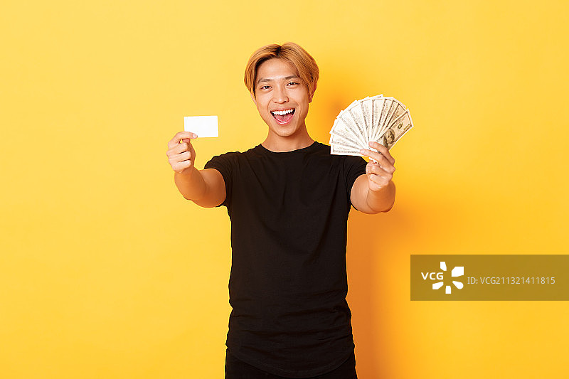 微笑年轻女人手持纸币信用卡肖像，黄色背景图片素材