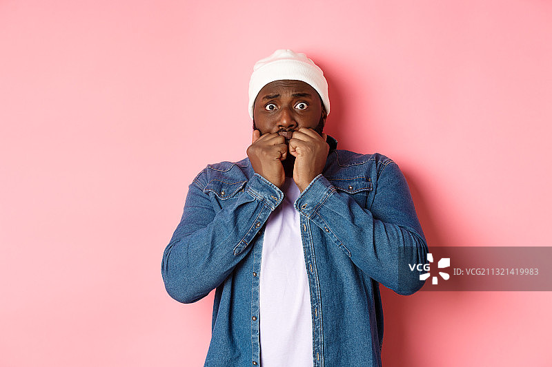 站在粉红色背景前，用手捂住脸的惊讶男子肖像图片素材