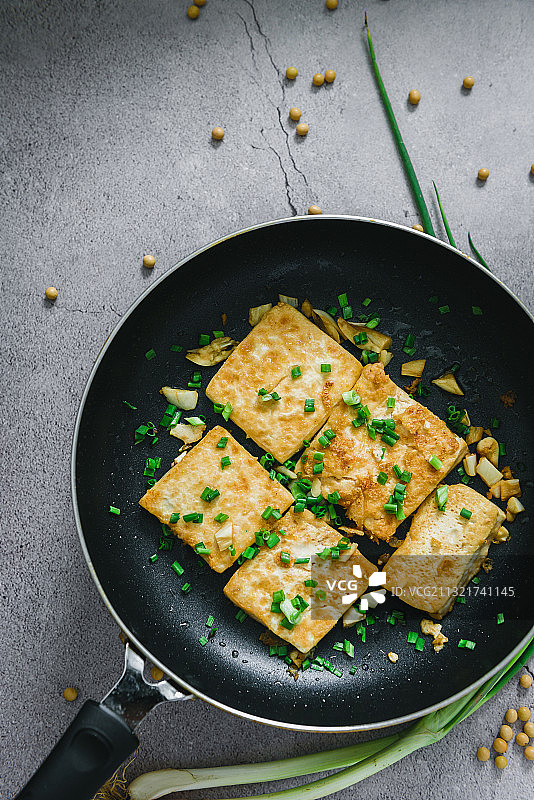 煎锅里面盛着几块煎熟的美味豆腐，豆腐上撒上了葱花图片素材