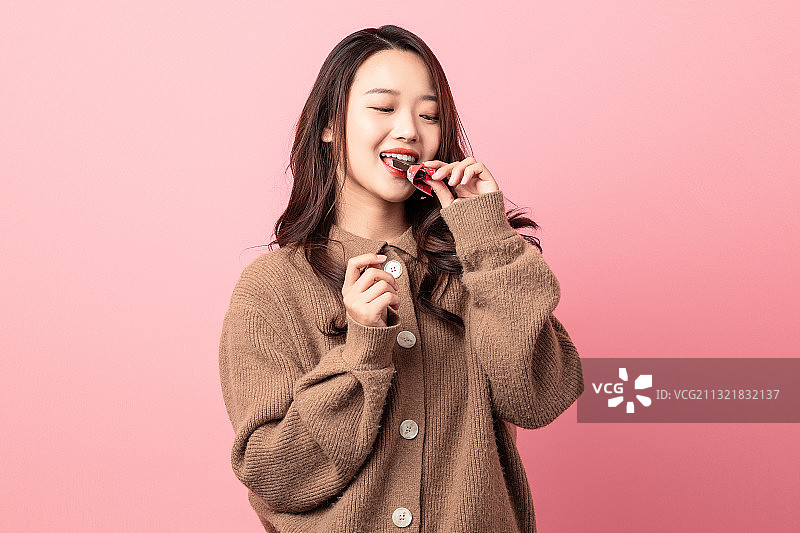 粉色背景里正在吃巧克力的美女图片素材