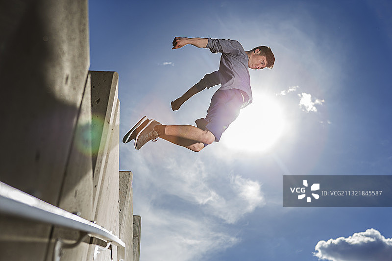 年轻男子在城市里做跑酷跳跃，蓝天图片素材