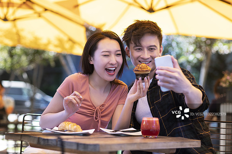 年轻情侣在户外咖啡厅用手机自拍图片素材