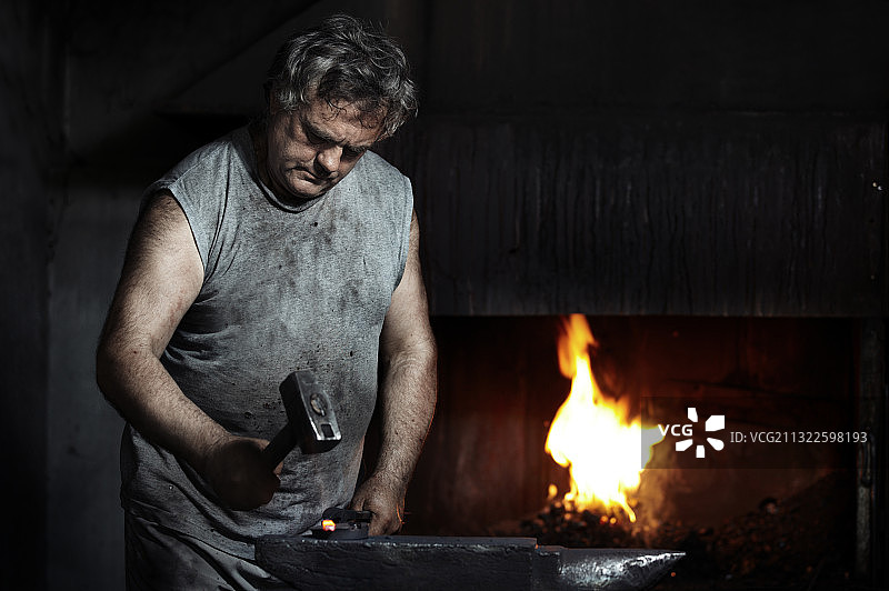 铁匠在燃烧的壁炉旁边的铁砧上锻造铁图片素材