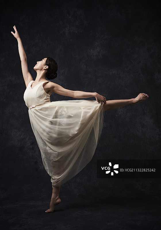 身穿白色连衣裙的女子在黑色背景中芭蕾舞，抬腿图片素材