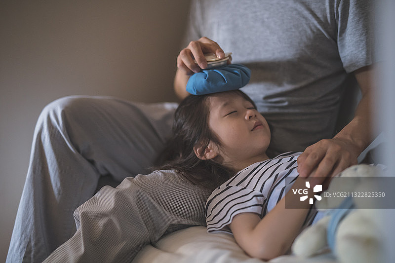 父亲把冰袋敷在躺在腿上的女儿身上图片素材